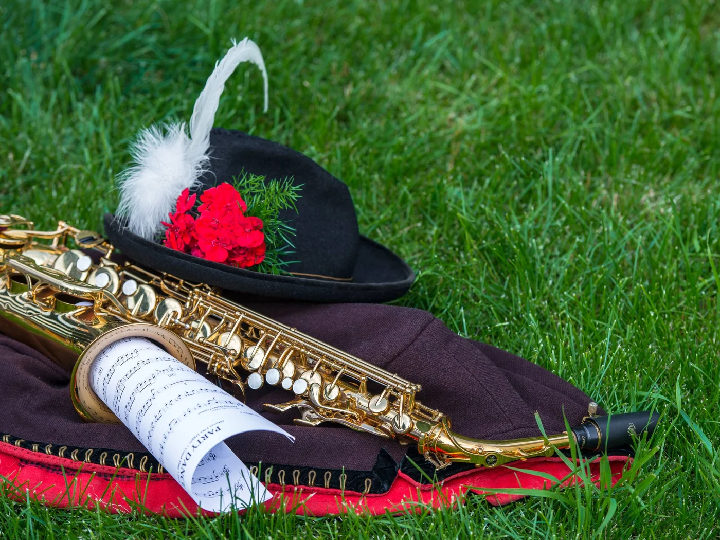 Saxophon, Notenblatt und Hut mit Feder und roten Blumen auf Gras