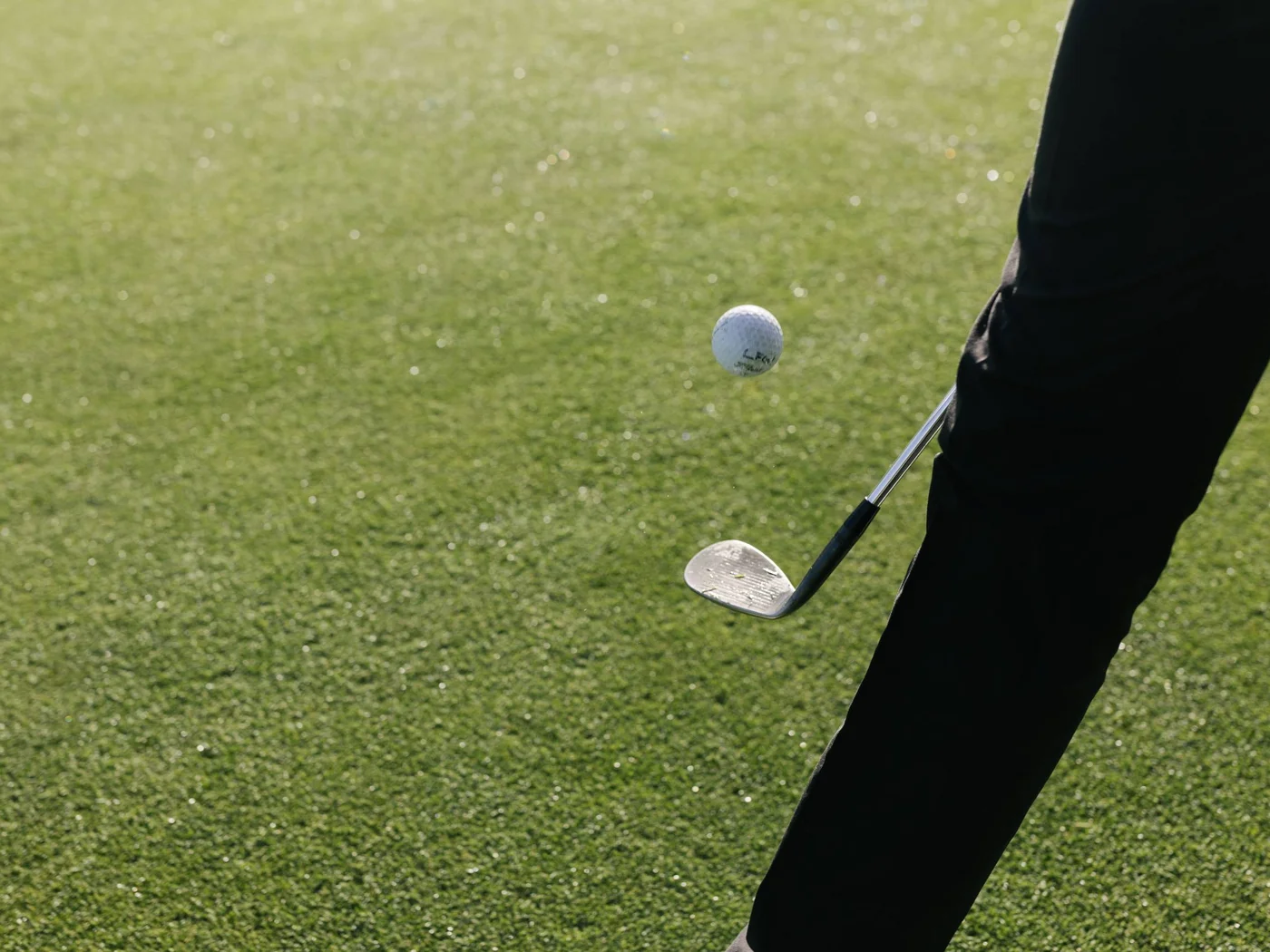 Person schlägt Golfball mit Golfschläger auf grünem Golfplatz