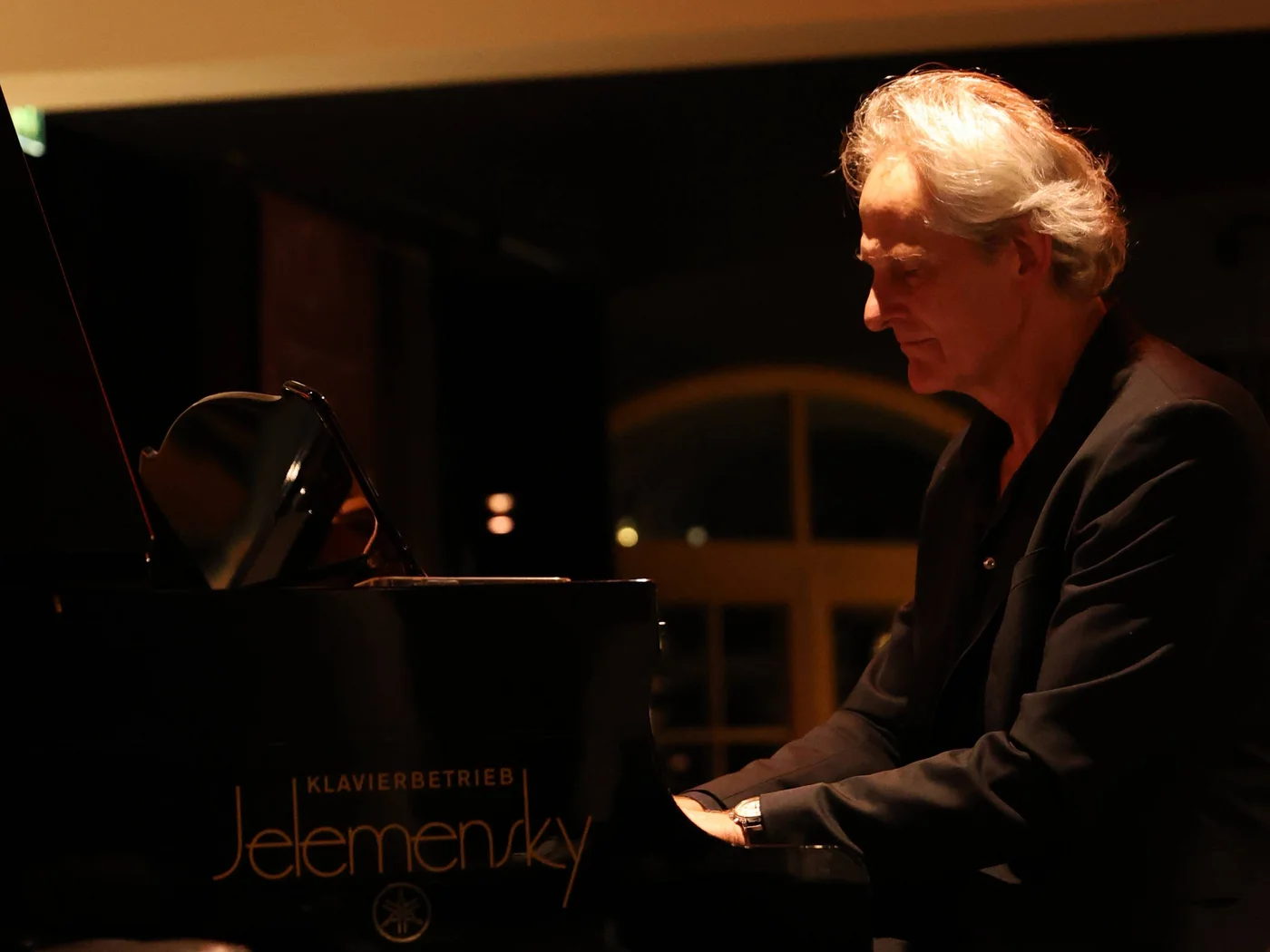 Die Schlossevents Älterer Mann spielt nachts Klavier in warmer Innenbeleuchtung