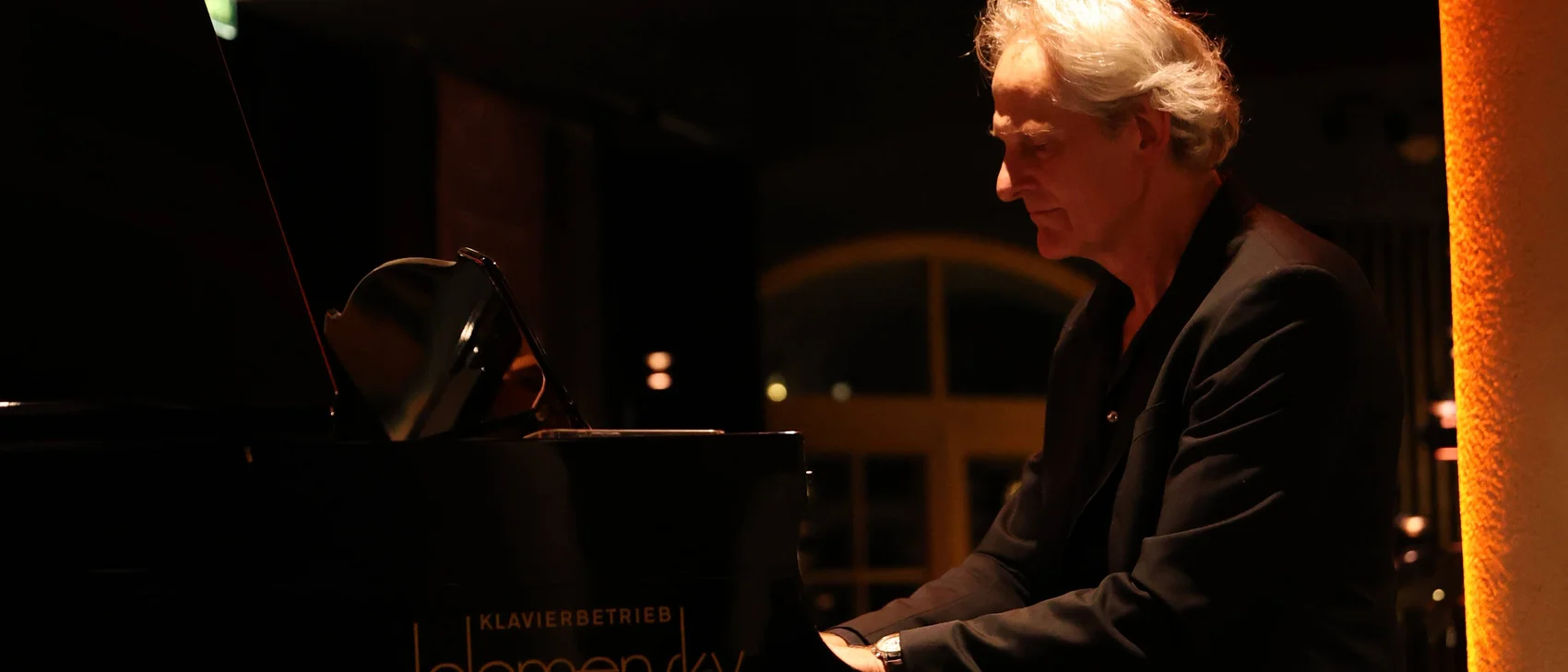 Älterer Mann spielt nachts Klavier in warmer Innenbeleuchtung